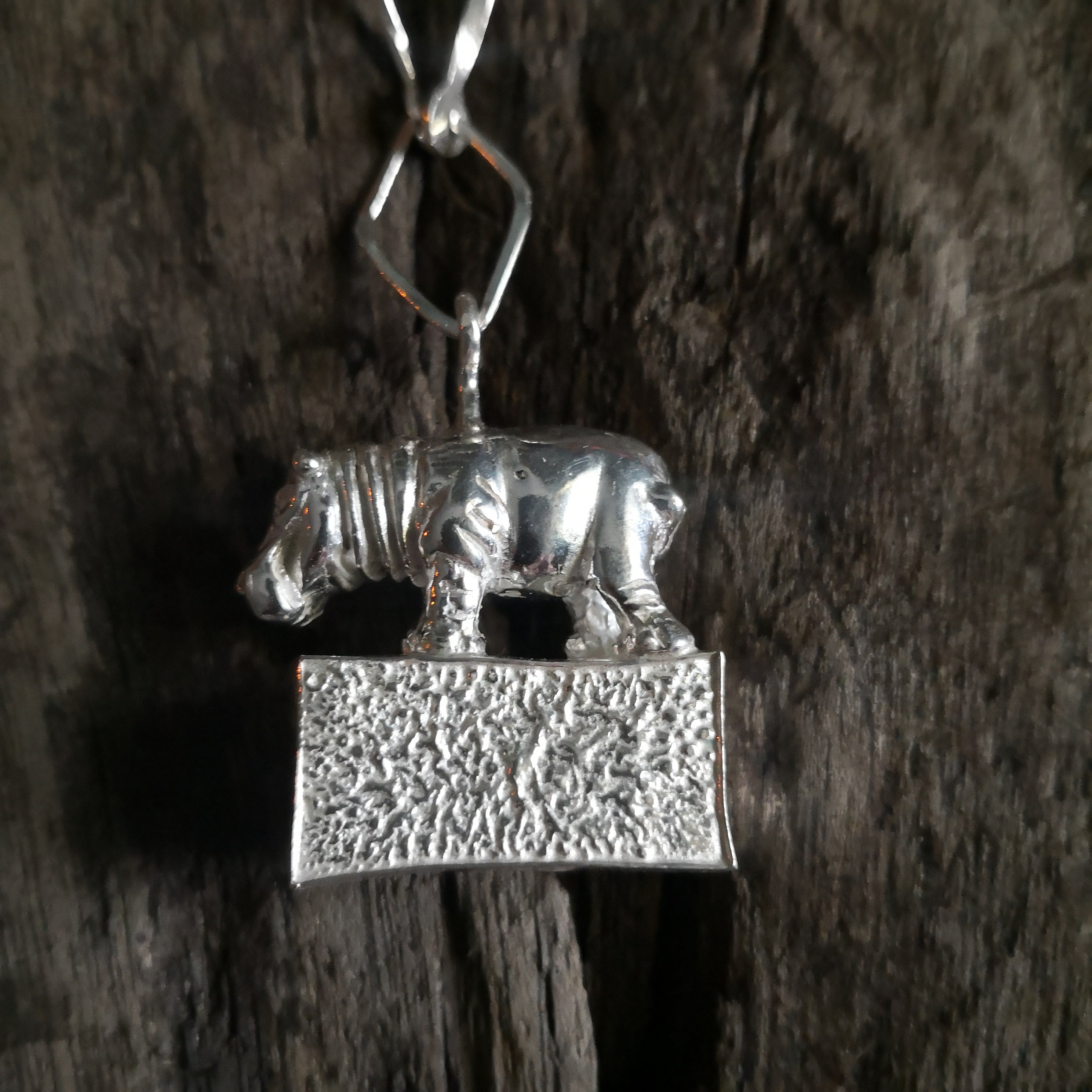 Hippo standing proudly on a hollow plinth suspended on a trapezoid chain. All hand crafted in sterling silver and hallmarked. 