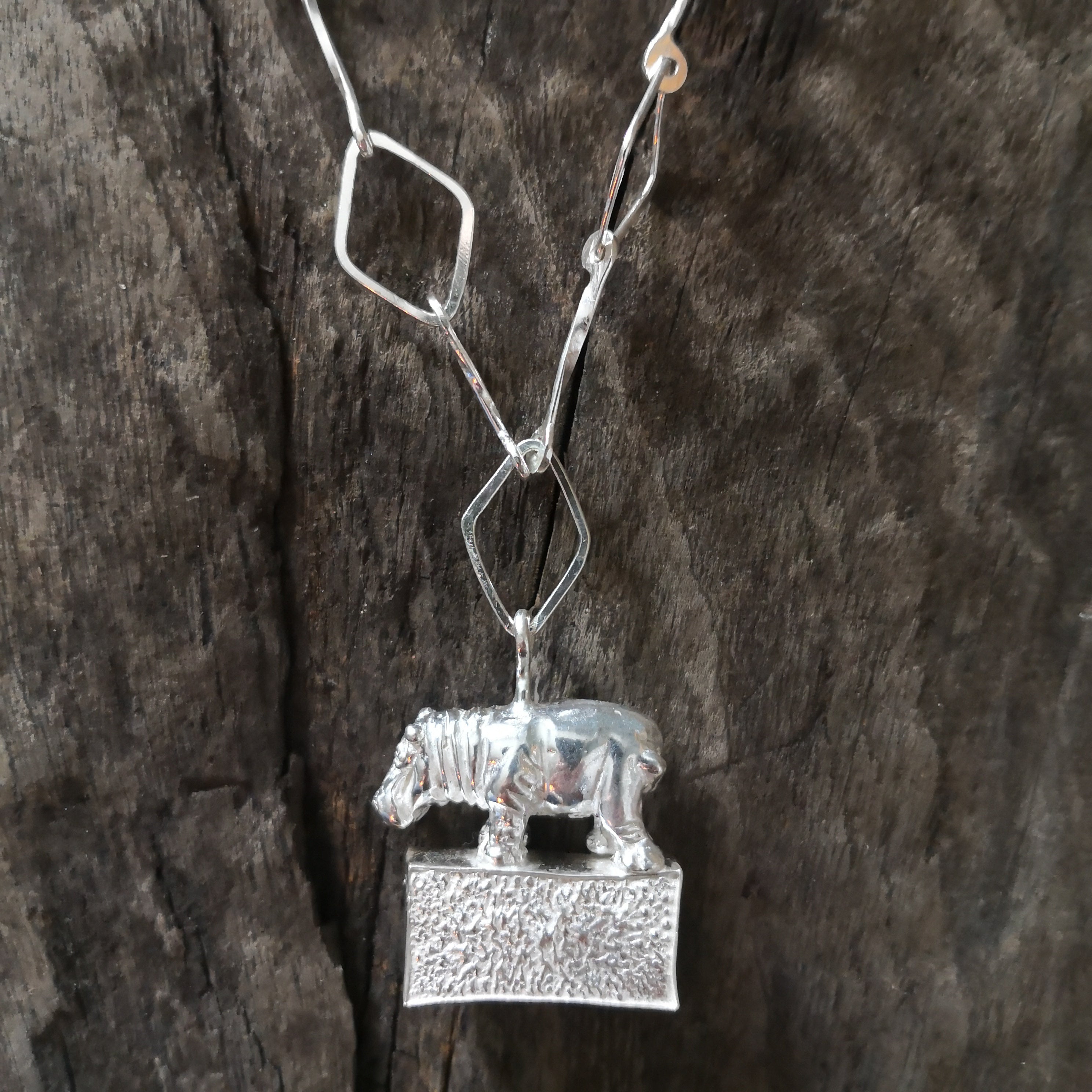 Hippo standing proudly on a hollow plinth suspended on a trapezoid chain. All hand crafted in sterling silver and hallmarked. 