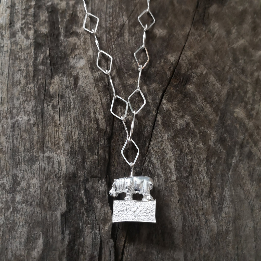 Hippo standing proudly on a hollow plinth suspended on a trapezoid chain. All hand crafted in sterling silver and hallmarked. 