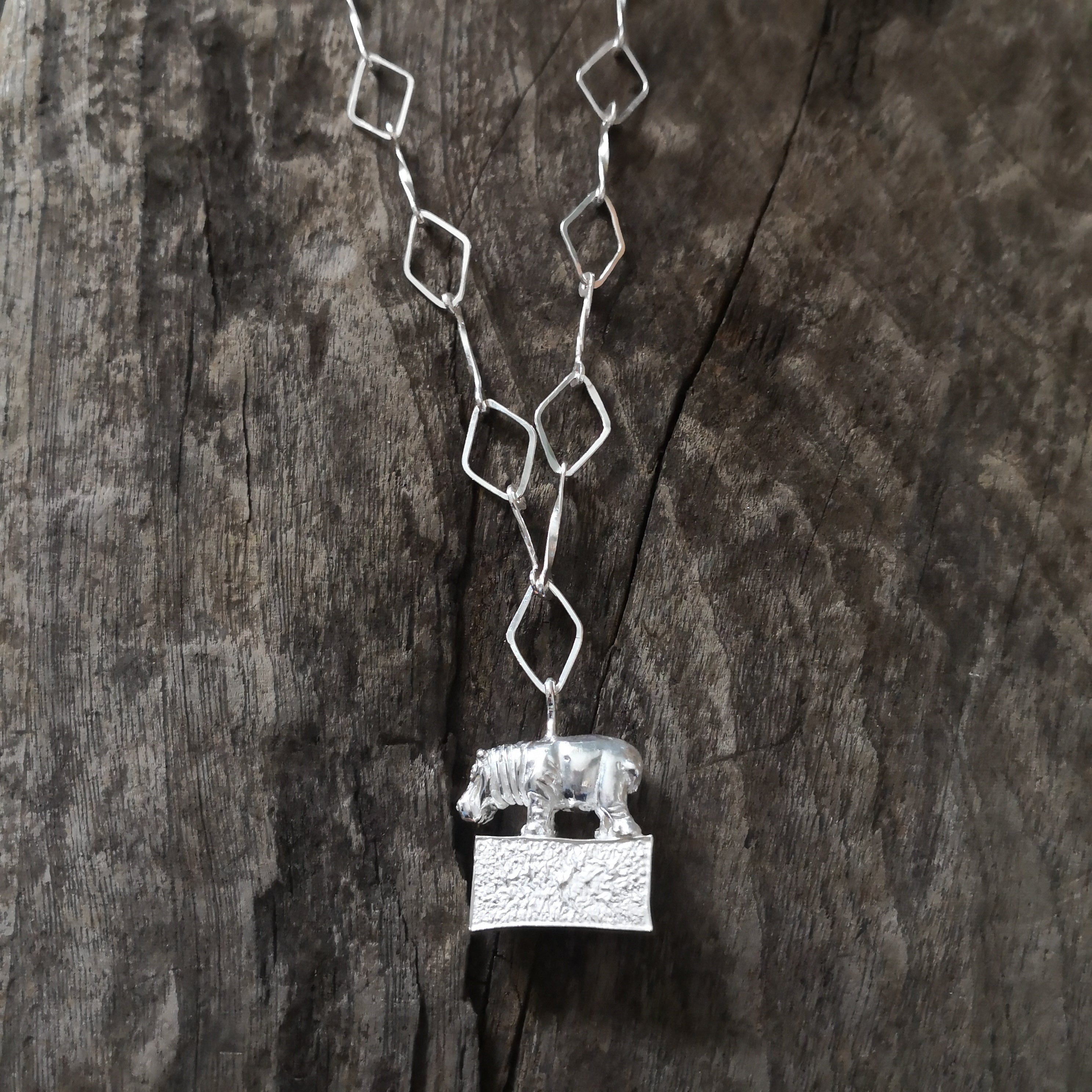 Hippo standing proudly on a hollow plinth suspended on a trapezoid chain. All hand crafted in sterling silver and hallmarked. 