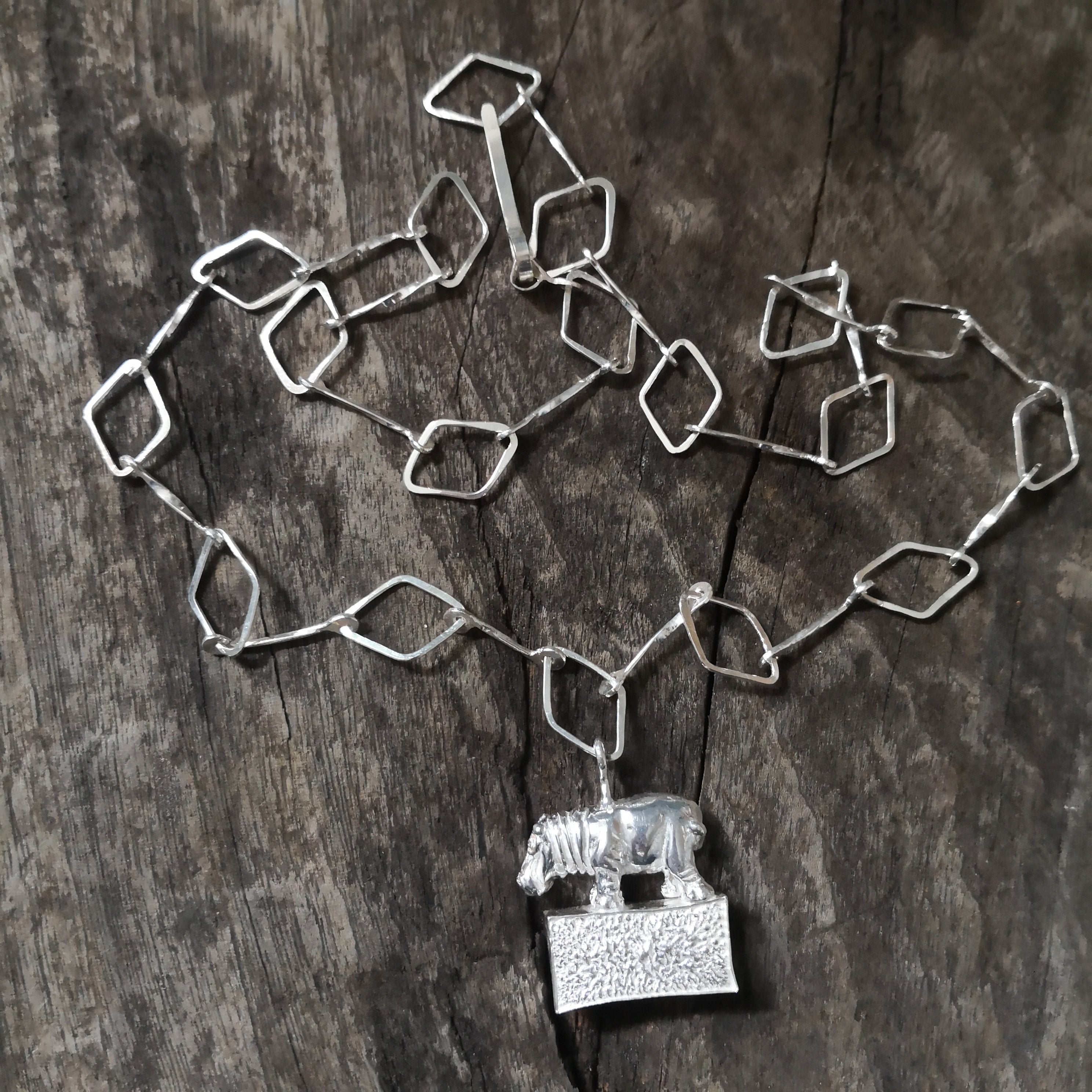 Hippo standing proudly on a hollow plinth suspended on a trapezoid chain. All hand crafted in sterling silver and hallmarked. 